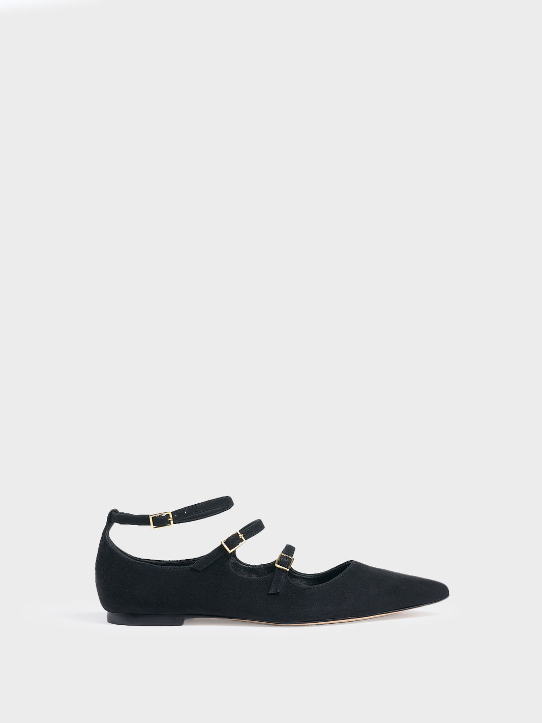 Profile view of a black suede mary jane flat with adjustable straps and a pointed toe. 