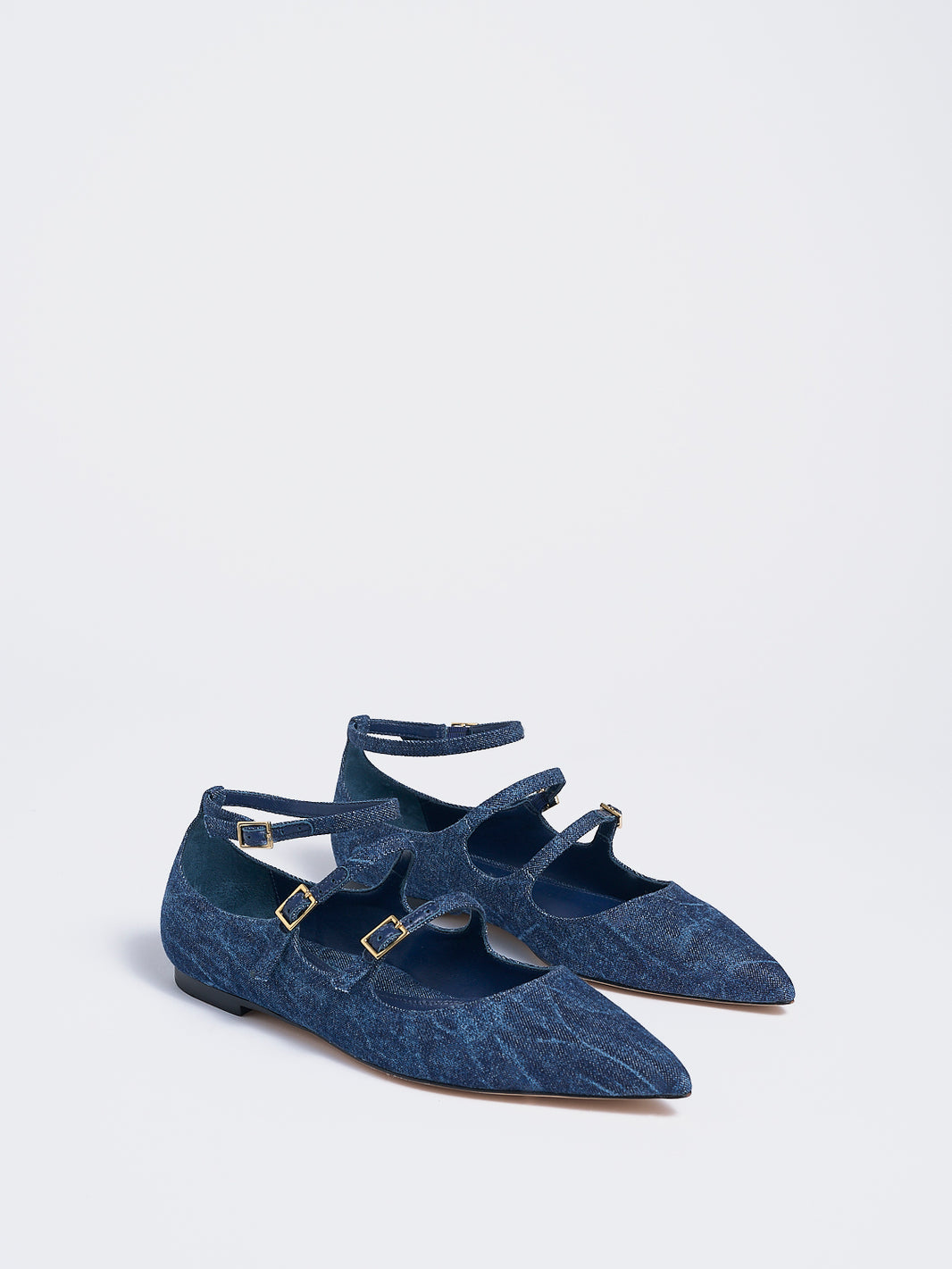 Angle view of a pair of navy denim mary jane flats with adjustable straps and a pointed toe. 