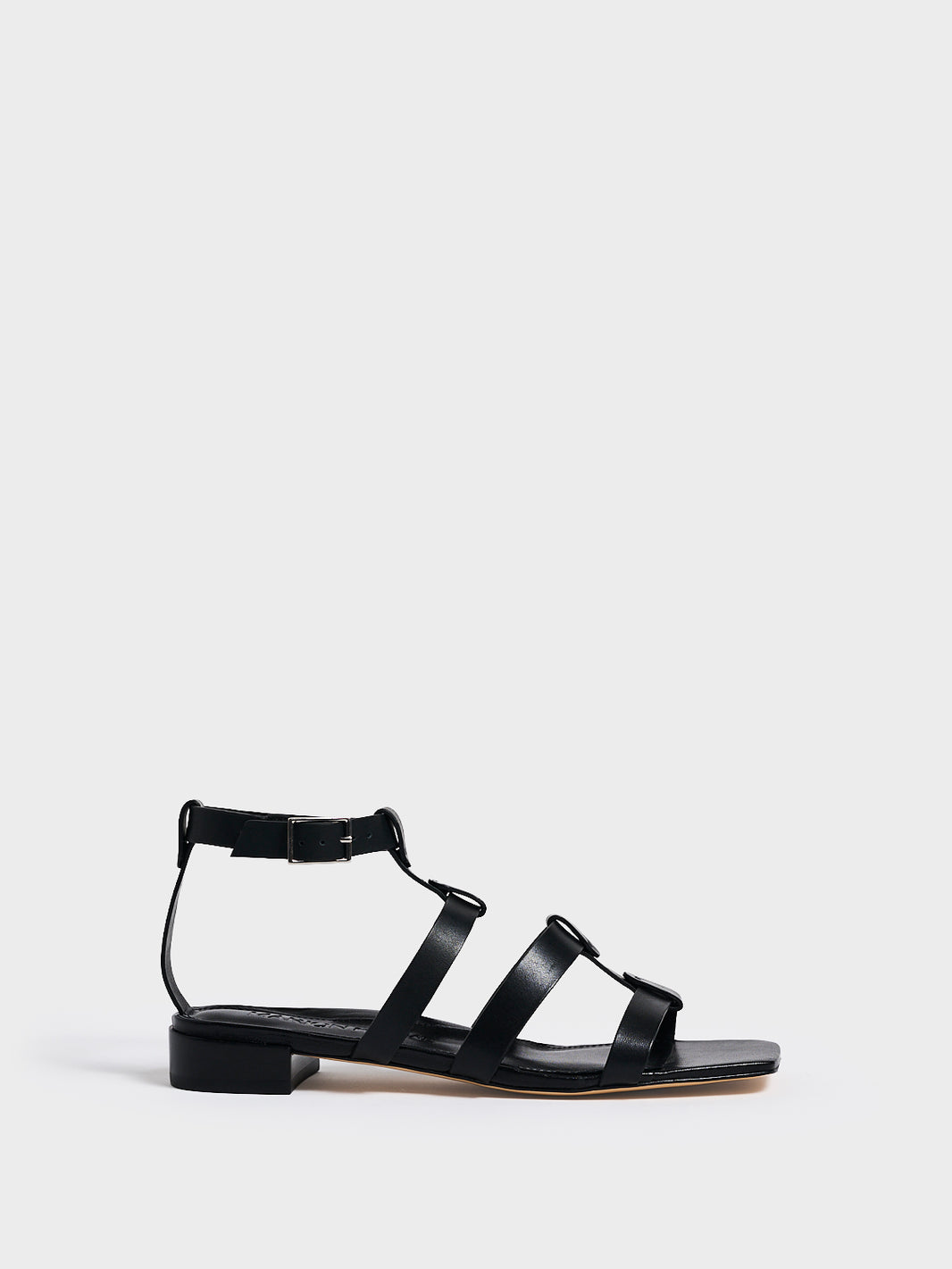 Profile view of an black leather gladiator sandal with an adjustable ankle strap.