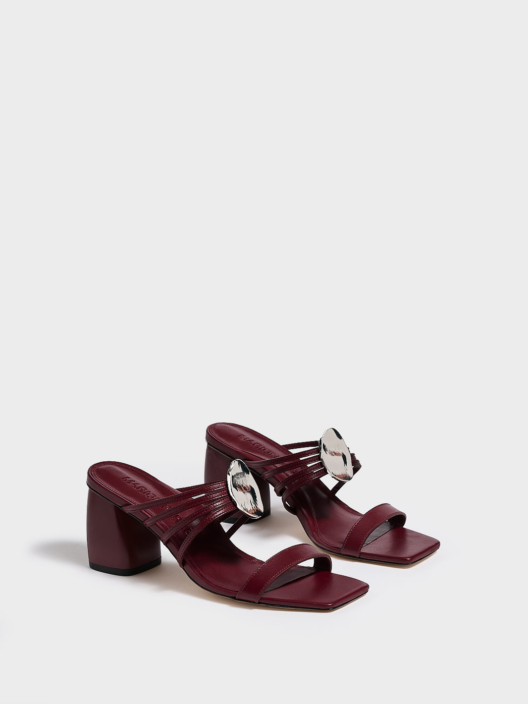 Angle view of a pair of burgundy leather block heel sandals with a strappy design and sculpted silver hardware.