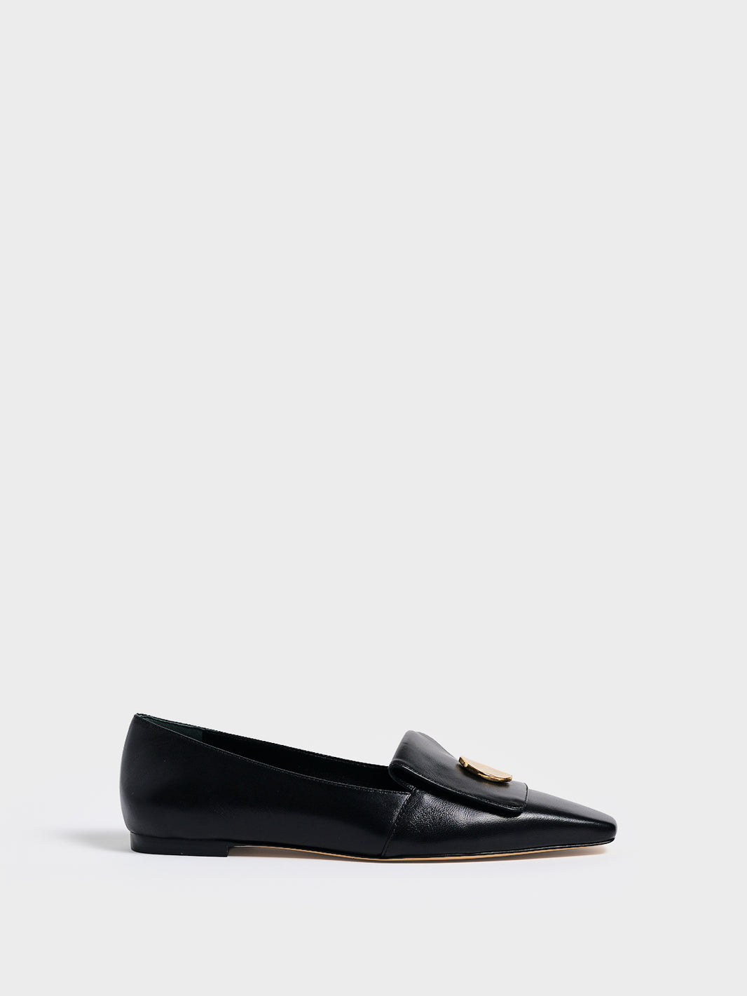 Profile view of a black leather flat  loafer with a  gold hardware detail and squared toe. 