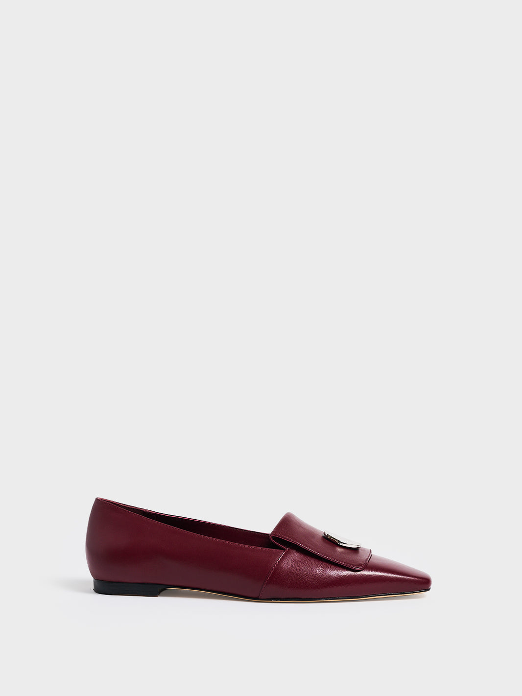 Profile view of a burgundy leather flat  loafer with a  silver hardware detail and squared toe. 