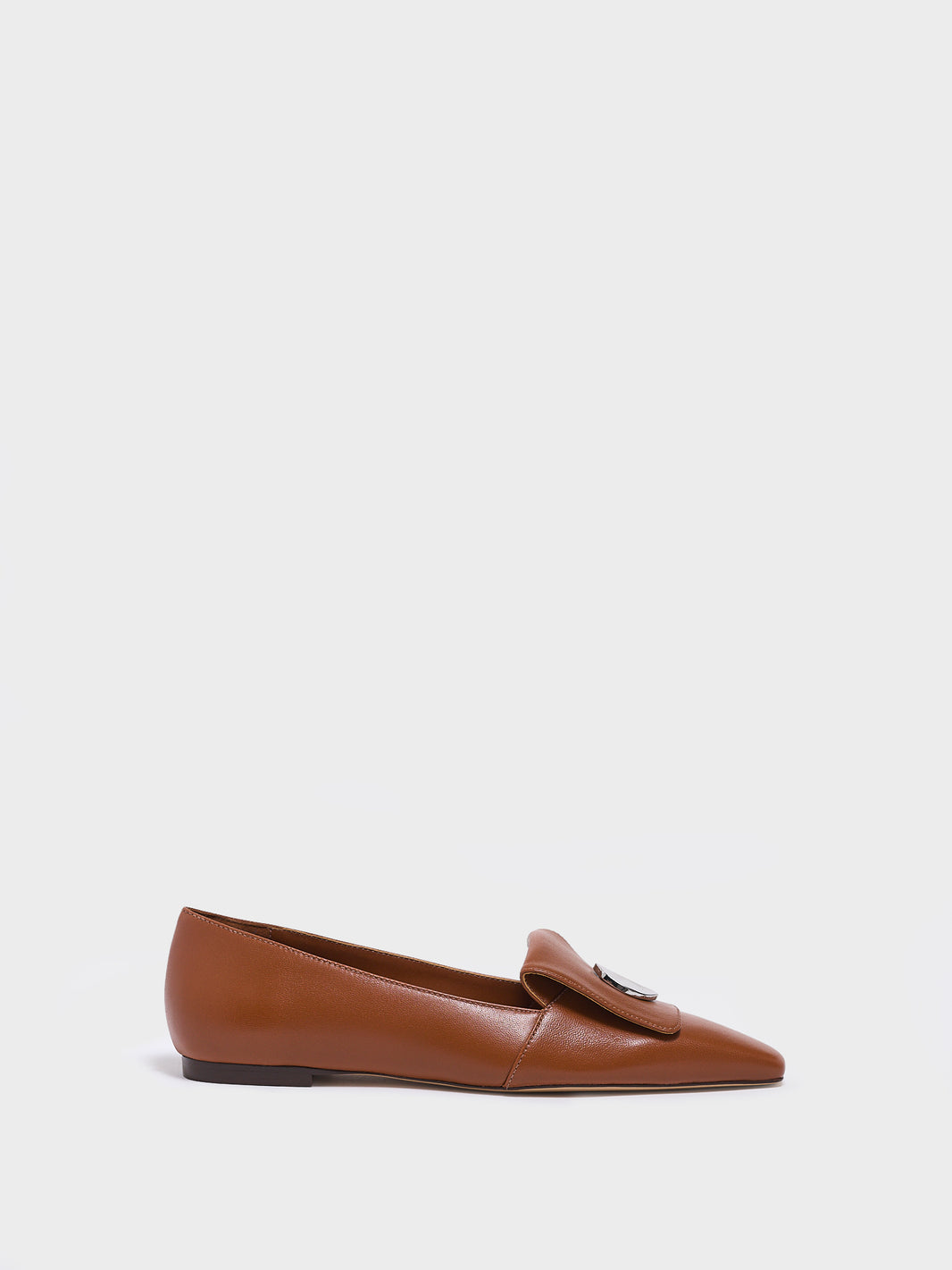 Profile view of a chestnut leather  flat loafer with a  silver hardware detail and squared toe. 