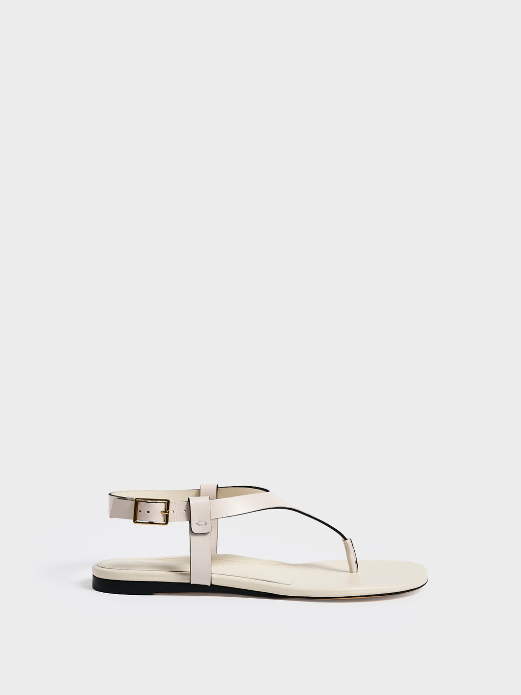 Profile view of a ivory leather thong sandal with a clean design and adjustable ankle strap. 