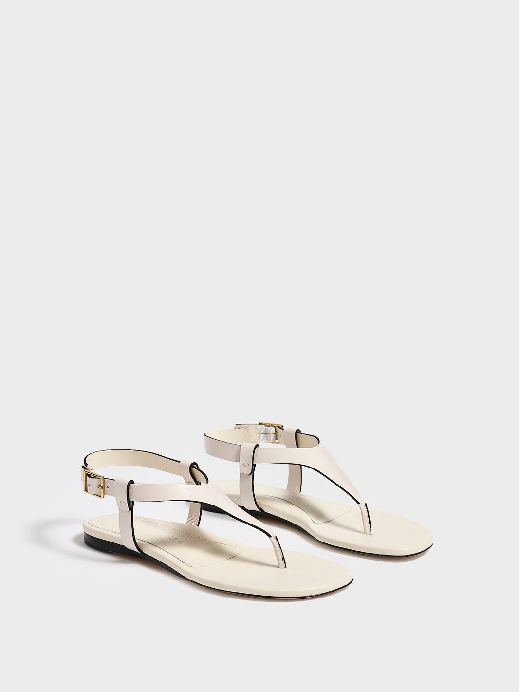 Angle view of a pair of ivory leather thong sandals with a clean design and adjustable ankle strap. 