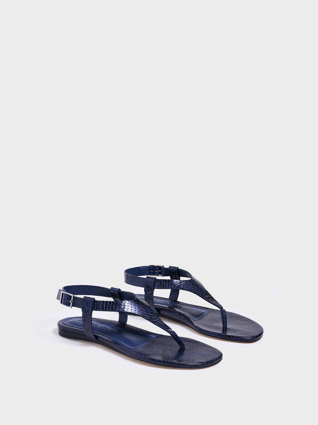 Angle view of a pair of navy python leather thong sandals with a clean design and adjustable ankle strap. 