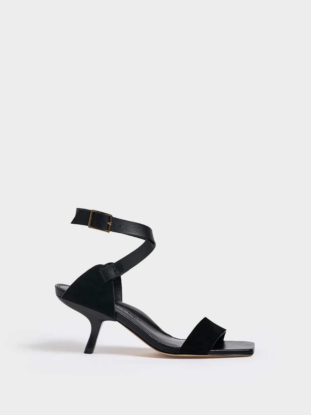 Profile view of a black leather and suede high heel sandal with a sculptural design and adjustable ankle strap. 