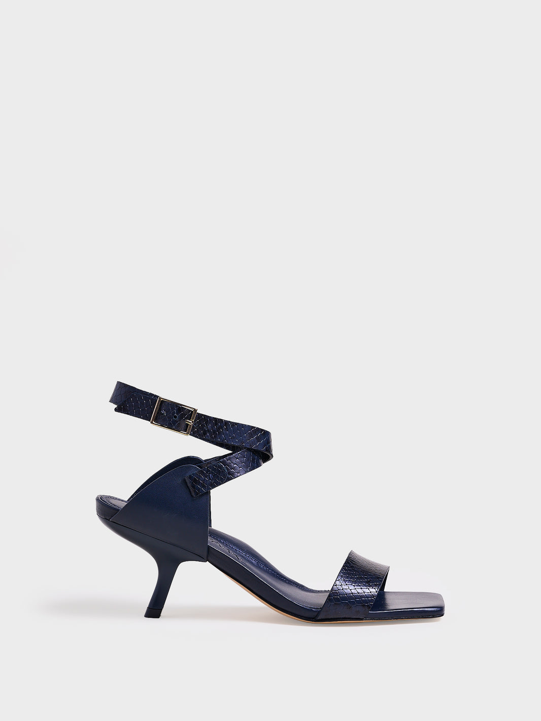Profile view of a navy python leather and suede high heel sandal with a sculptural design and adjustable ankle strap. 