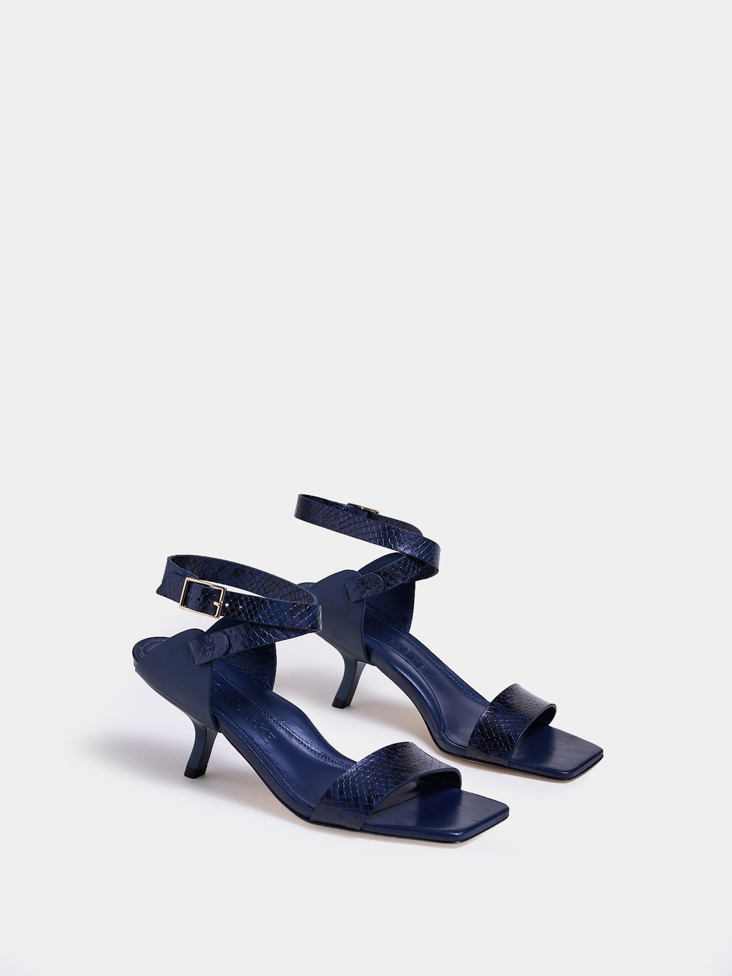 Angle view of a pair of navy python leather and suede high heel sandals with a sculptural design and adjustable ankle strap. 